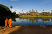 Classic view of Angkor Wat across the pools with a clear reflection, with two orange-robed monks in the foreground