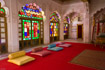 Gaudy room in the palace at Jodhpur with carved stonework and coloured glass above a red carpet and colourful cushions
