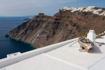 A small, weathered rowing boat used as a picturesque ornament on a flat white roof with the caldera cliffs in the background on Santorini